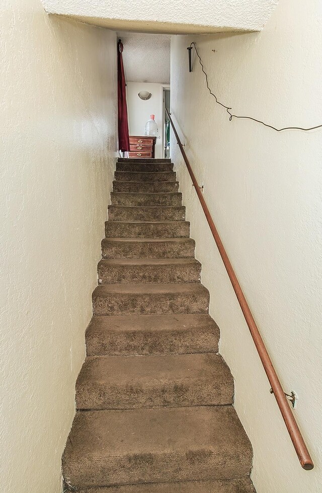 staircase featuring a textured ceiling and a textured wall