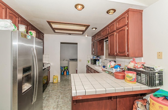 kitchen featuring tile counters, light tile patterned floors, decorative backsplash, a peninsula, and stainless steel fridge