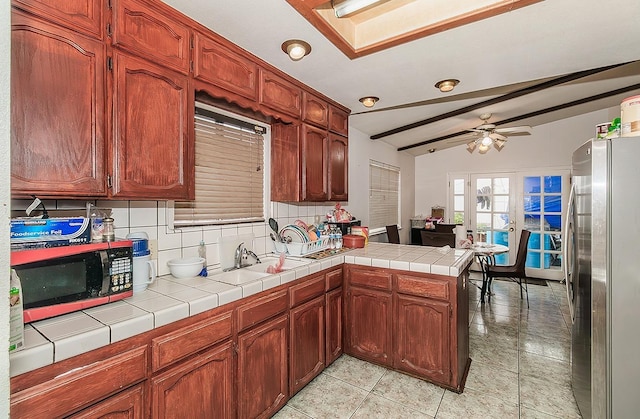 kitchen with a ceiling fan, a peninsula, vaulted ceiling with beams, freestanding refrigerator, and backsplash