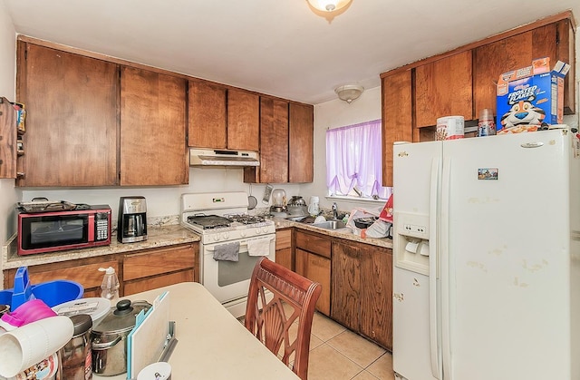 kitchen with under cabinet range hood, brown cabinets, light tile patterned flooring, white appliances, and a sink