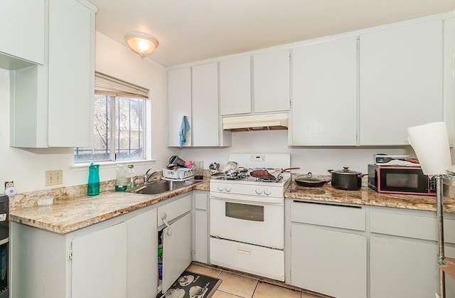 kitchen with white gas stove, under cabinet range hood, a sink, light tile patterned flooring, and light countertops