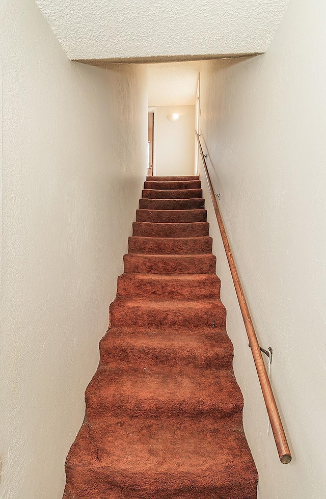 staircase with a textured ceiling and a textured wall