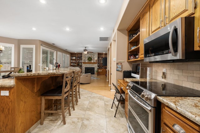 kitchen featuring visible vents, a ceiling fan, a kitchen breakfast bar, backsplash, and appliances with stainless steel finishes