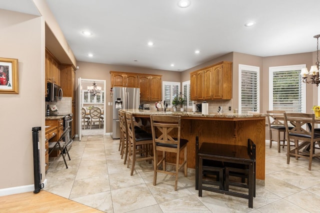 kitchen featuring light stone counters, a peninsula, a breakfast bar area, appliances with stainless steel finishes, and a chandelier