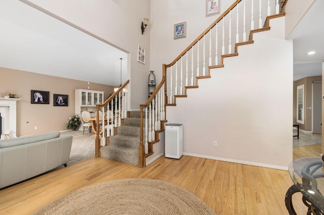 stairs featuring baseboards, a fireplace, wood finished floors, and a towering ceiling