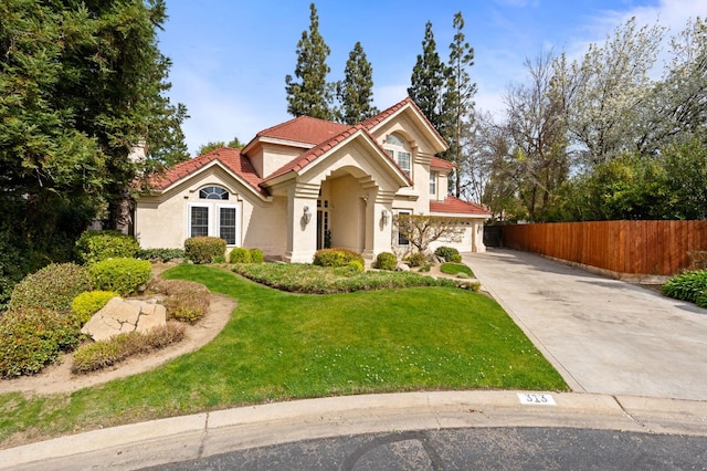 mediterranean / spanish-style home with stucco siding, driveway, a tile roof, fence, and a front yard