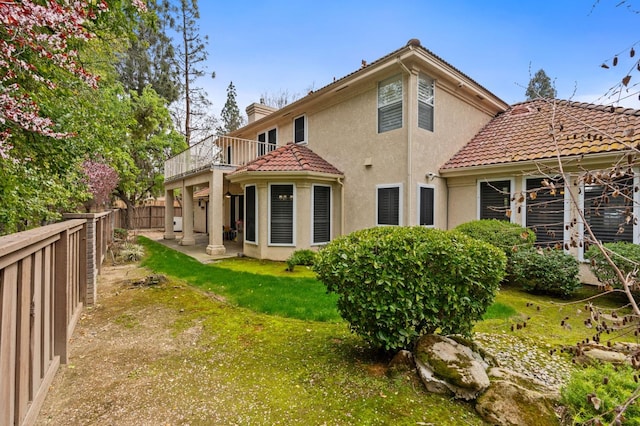 back of property with a balcony, a yard, a fenced backyard, stucco siding, and a chimney