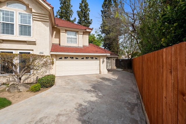 exterior space featuring stucco siding, fence, concrete driveway, and a tiled roof