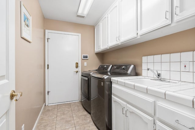 laundry area featuring light tile patterned floors, baseboards, washing machine and clothes dryer, cabinet space, and a sink