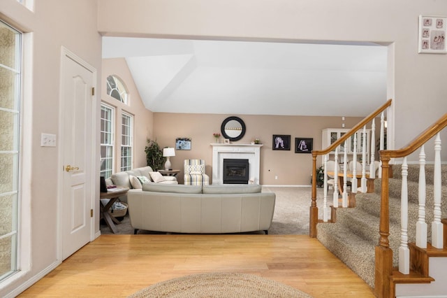 living area with vaulted ceiling, stairway, wood finished floors, and a glass covered fireplace