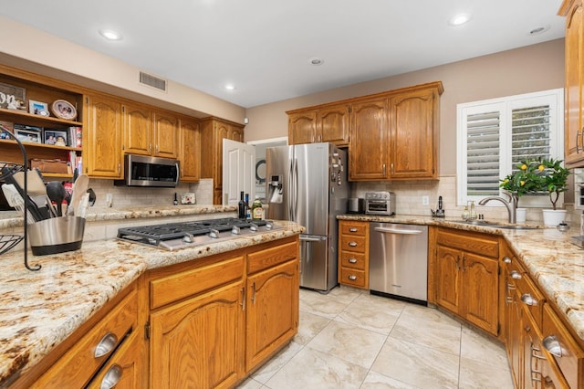 kitchen featuring visible vents, a sink, appliances with stainless steel finishes, brown cabinets, and backsplash