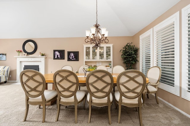 dining space with light carpet, a notable chandelier, a tile fireplace, and lofted ceiling