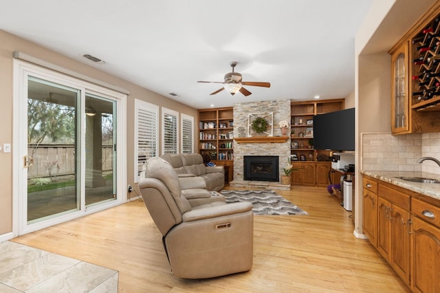 living room featuring ceiling fan, visible vents, light wood-style flooring, and a fireplace