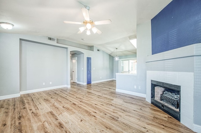 unfurnished living room with visible vents, a tiled fireplace, wood finished floors, arched walkways, and vaulted ceiling