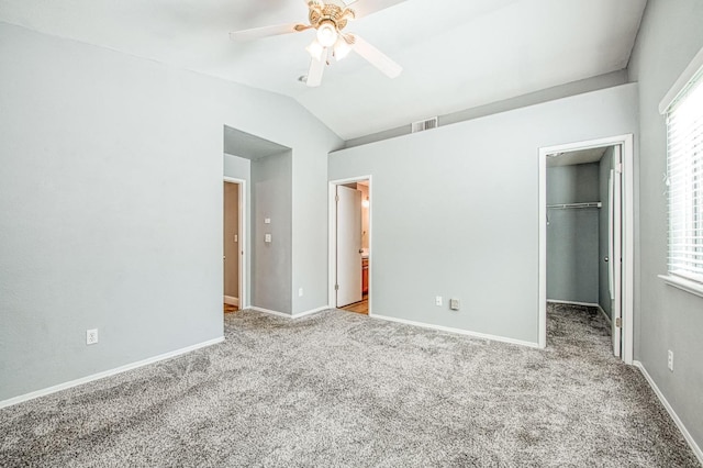 unfurnished bedroom with baseboards, lofted ceiling, a spacious closet, carpet flooring, and multiple windows