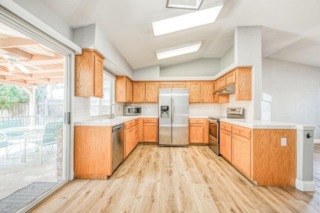 kitchen featuring light wood finished floors, under cabinet range hood, tile countertops, lofted ceiling, and appliances with stainless steel finishes