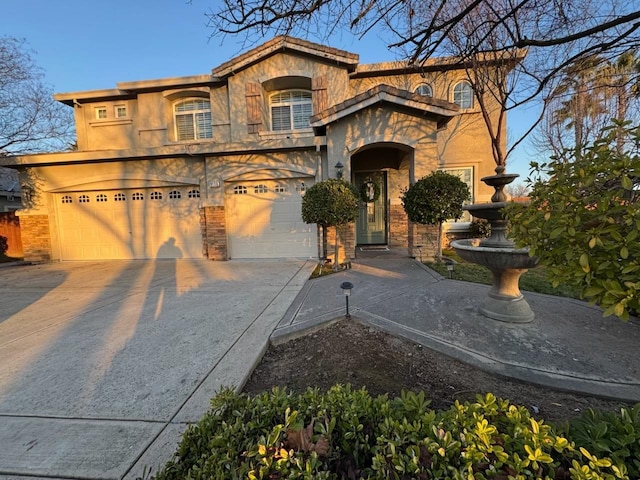 mediterranean / spanish-style house featuring stone siding, stucco siding, an attached garage, and concrete driveway