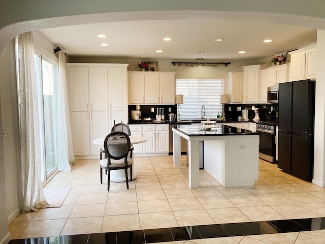 kitchen with light tile patterned floors, a kitchen island, dark countertops, and appliances with stainless steel finishes