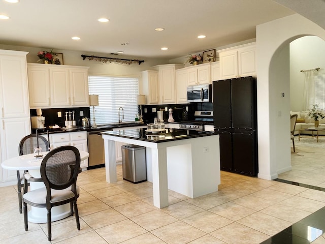 kitchen with a kitchen island, light tile patterned flooring, arched walkways, stainless steel appliances, and dark countertops