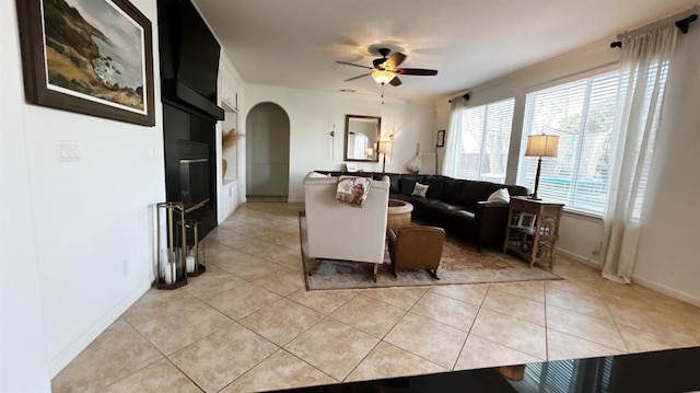 living room featuring ceiling fan, baseboards, arched walkways, and light tile patterned flooring