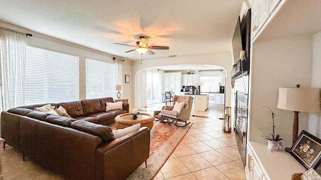 living area featuring arched walkways, a textured ceiling, light tile patterned flooring, and a ceiling fan