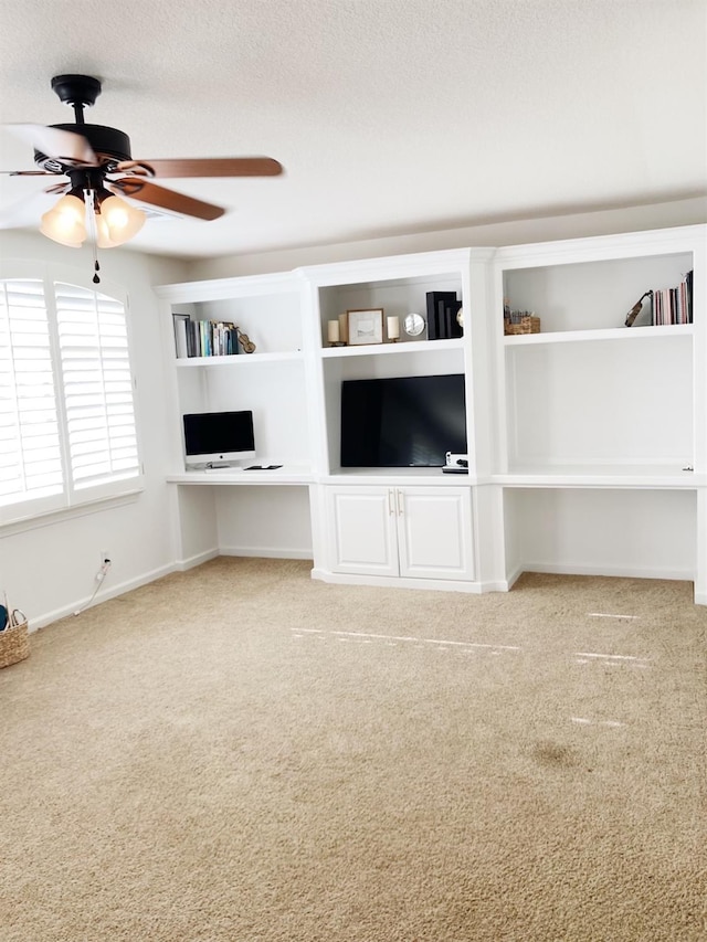 unfurnished living room featuring a textured ceiling, built in desk, carpet, baseboards, and ceiling fan