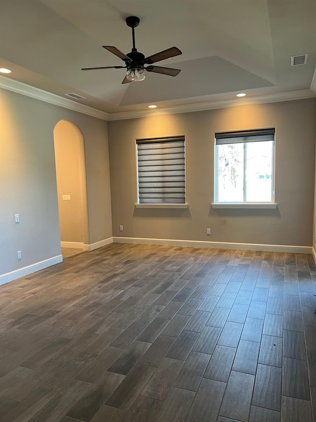 unfurnished room featuring a tray ceiling, arched walkways, dark wood finished floors, and crown molding