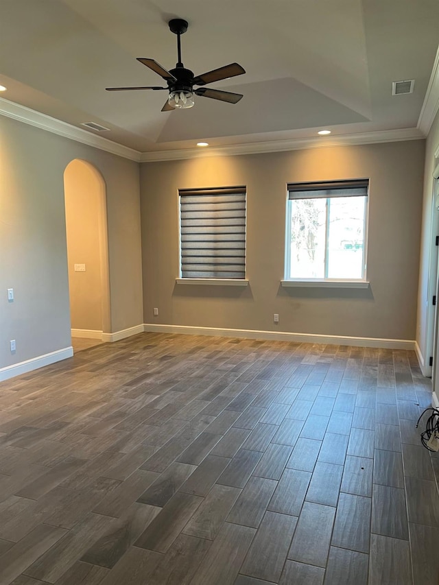 empty room with arched walkways, dark wood-style flooring, a raised ceiling, and ornamental molding