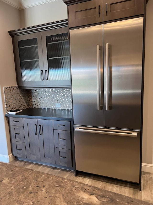 kitchen with baseboards, ornamental molding, built in fridge, dark countertops, and tasteful backsplash