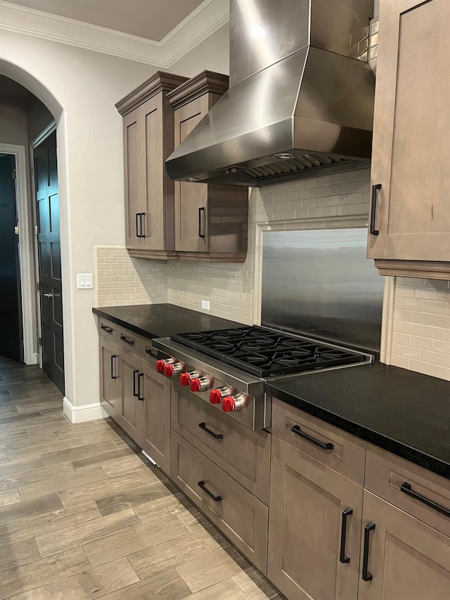 kitchen featuring light wood-type flooring, ornamental molding, dark countertops, wall chimney exhaust hood, and stainless steel gas cooktop