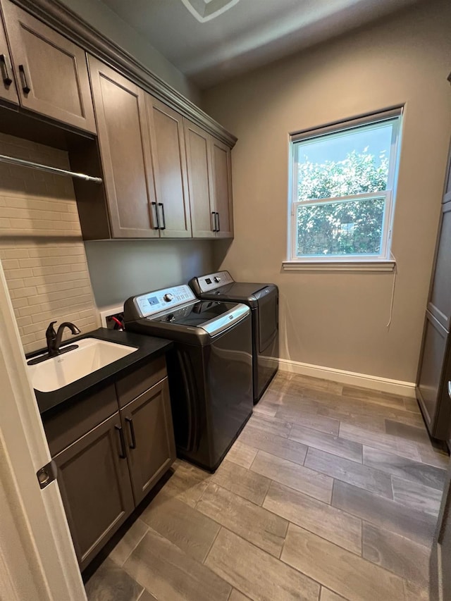 laundry area featuring a sink, washing machine and dryer, cabinet space, light wood-style floors, and baseboards