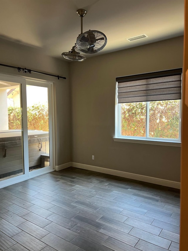 spare room featuring visible vents, baseboards, a healthy amount of sunlight, and wood finished floors