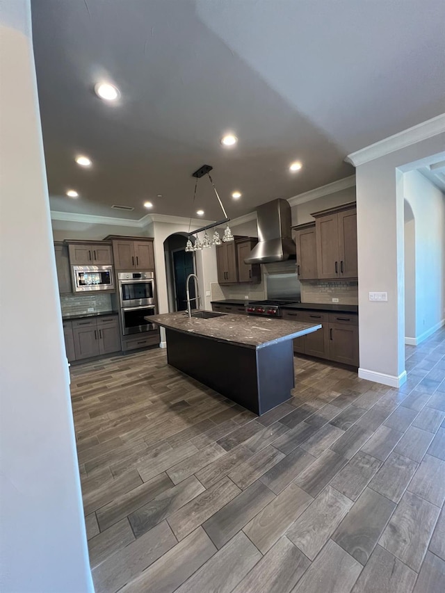 kitchen featuring decorative backsplash, wall chimney exhaust hood, arched walkways, and a sink