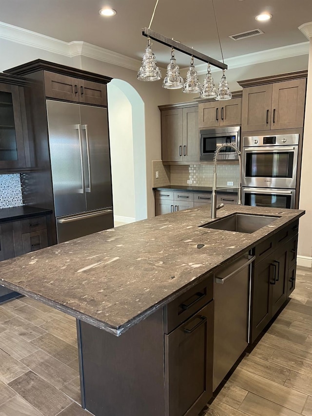 kitchen with arched walkways, built in appliances, backsplash, and crown molding