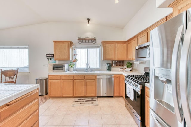 kitchen with a sink, lofted ceiling, appliances with stainless steel finishes, and tile countertops