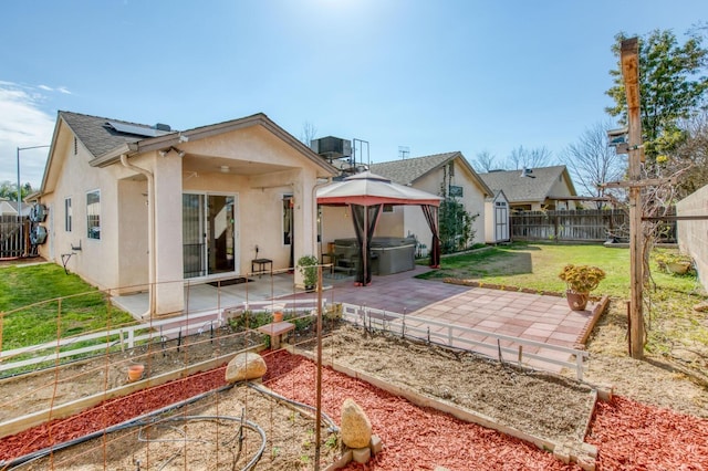 back of house featuring stucco siding, a hot tub, a gazebo, a patio area, and roof mounted solar panels