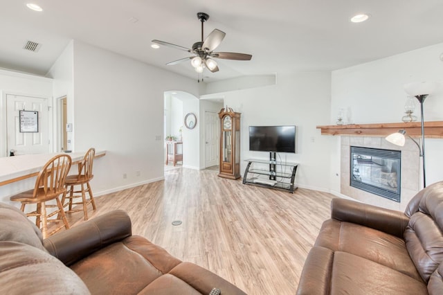 living room with light wood-type flooring, visible vents, a ceiling fan, arched walkways, and a tile fireplace