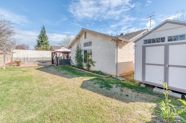 view of side of property featuring a storage unit, a fenced backyard, a gazebo, a yard, and an outdoor structure