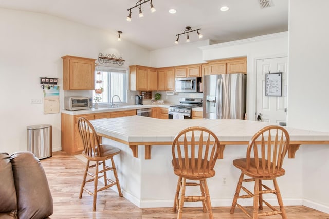 kitchen with tile counters, appliances with stainless steel finishes, a breakfast bar, and a sink