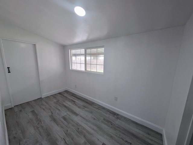 spare room featuring vaulted ceiling, wood finished floors, and baseboards