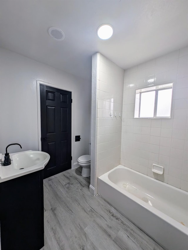 full bath with toilet, wood finished floors, washtub / shower combination, baseboards, and vanity