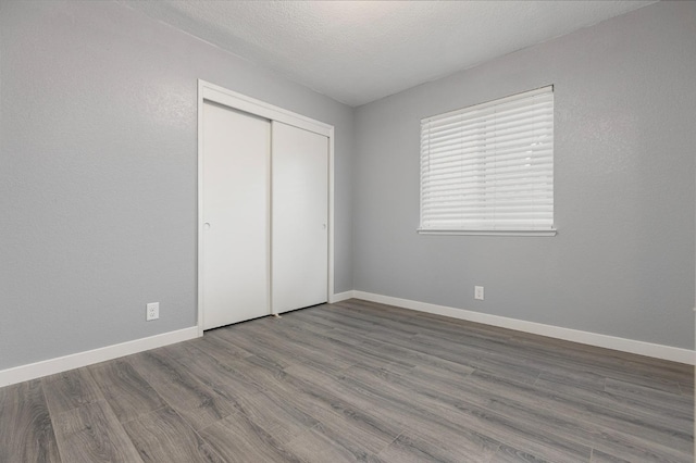 unfurnished bedroom featuring a closet, a textured ceiling, baseboards, and wood finished floors