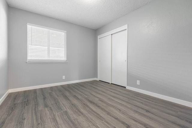 unfurnished bedroom with a textured ceiling, wood finished floors, a closet, and baseboards