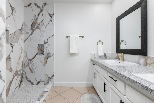 bathroom with a sink, a marble finish shower, tile patterned flooring, double vanity, and baseboards