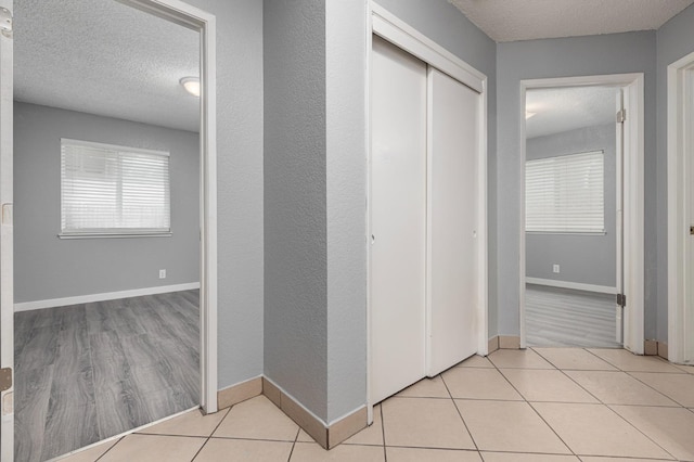 hallway with tile patterned floors, baseboards, and a textured ceiling