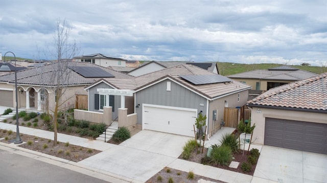 view of front of property with solar panels, an attached garage, fence, a tiled roof, and driveway