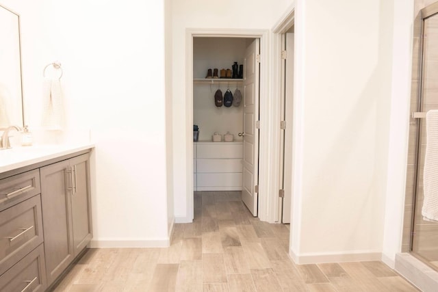 bathroom featuring a walk in closet, vanity, a stall shower, and baseboards