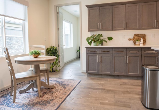 kitchen with baseboards, light wood-style flooring, light countertops, dark brown cabinetry, and backsplash