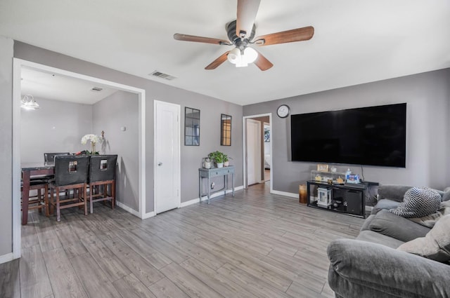 living room with light wood finished floors, visible vents, ceiling fan, and baseboards