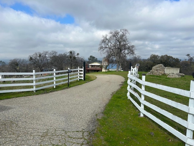 view of gate featuring a rural view, a lawn, and fence